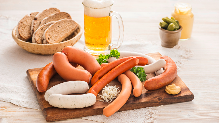 Diverse Würste auf Holzbrett serviert, mit Brotkorb und Bier